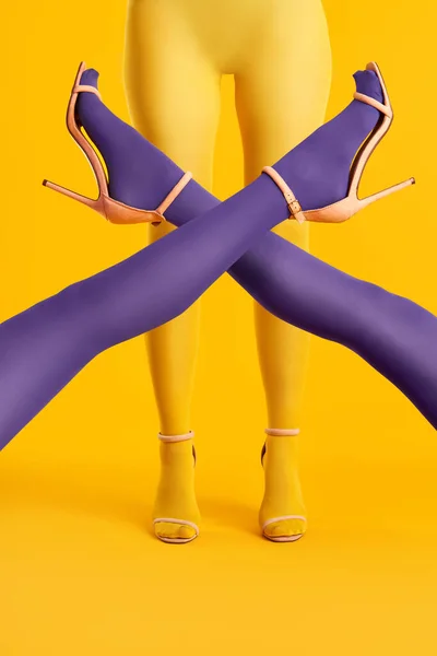 Largas piernas delgadas cruzadas de mujeres jóvenes en medias púrpuras posando sobre mujer en medias amarillas —  Fotos de Stock