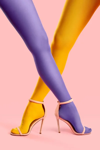 Long slim crossed legs of young women in yellow and purple tights posing on pink background