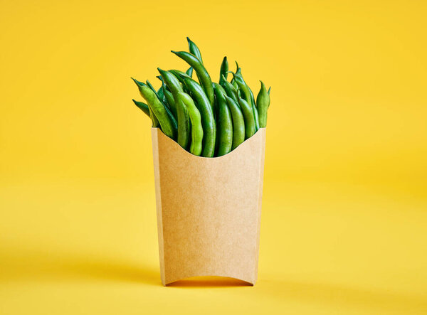 зеленая фасоль в бумажной коробке быстрого питания на ярко-желтом фоне с копировальным пространством