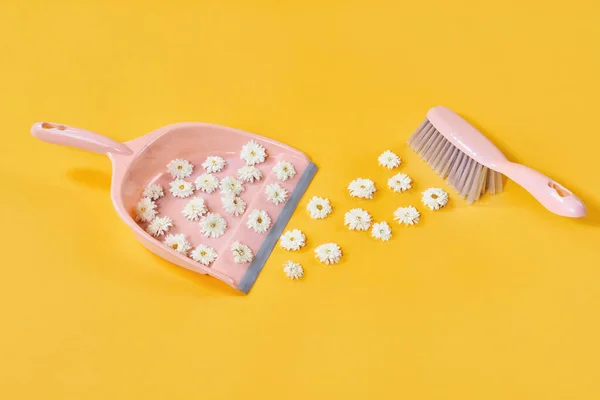 Sweeping white flowers in brush and dustpan on yellow studio background — Stockfoto