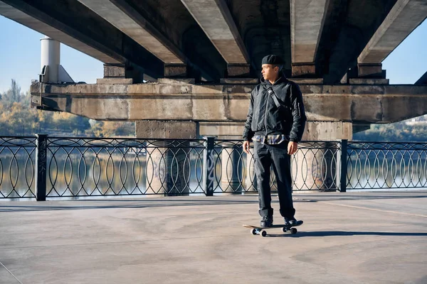 Skater fährt auf Skateboard auf leerem Betondamm vor städtischem Hintergrund — Stockfoto