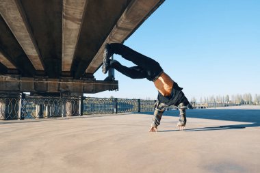 Genç break dansçı, takla atarak akrobatik hareketler yapıyor. Şehir arka planında dans ediyor.