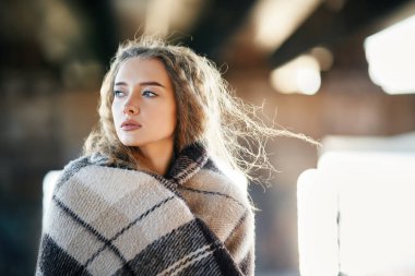 Şehir arka planında yün battaniyeye sarılı güzel düşünceli bir kadının portresi.