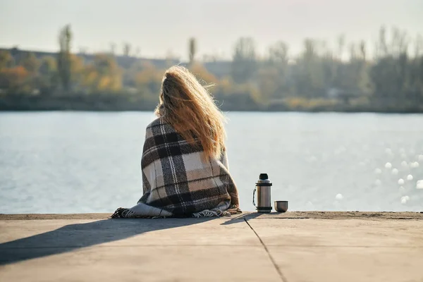 Woman relaxing alone by a river in the city wrapped in wool blanket enjoying nature — Stock Photo, Image