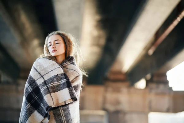 Portrait de jolie femme réfléchie enveloppée dans une couverture en laine posant sur fond urbain — Photo