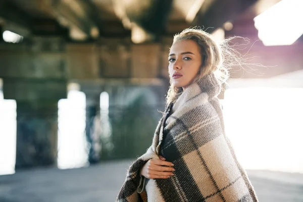 Портрет досить впевненої жінки, загорнутої у вовняну ковдру, яка дивиться на камеру, позуючи на міському вуличному тлі з копіювальним простором — стокове фото