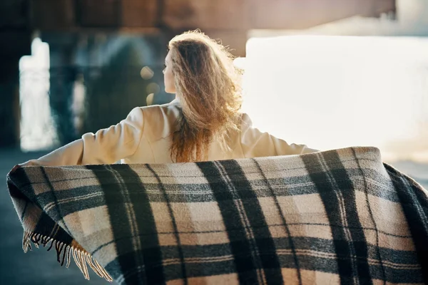 Вид сзади на молодую женщину с одеялом, наслаждающуюся ветреным солнечным днем, позирующую на фоне городской улицы. — стоковое фото