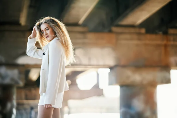 Retrato de una hermosa joven posando sobre un fondo urbano mirando a la cámara en un día soleado y ventoso —  Fotos de Stock