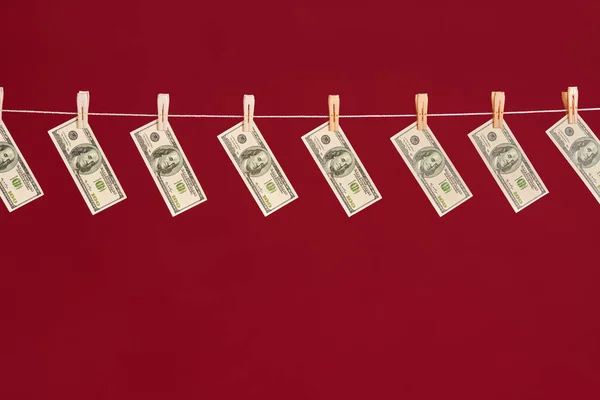 Ξέπλυμα χρήματος, δολάρια ΗΠΑ κρέμονται σε σχοινί πάνω από το κόκκινο φόντο στούντιο — Φωτογραφία Αρχείου