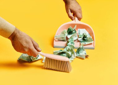 Erkek eli ile yaratıcı düzen sarı arka planda dolar banknotları süpürüyor