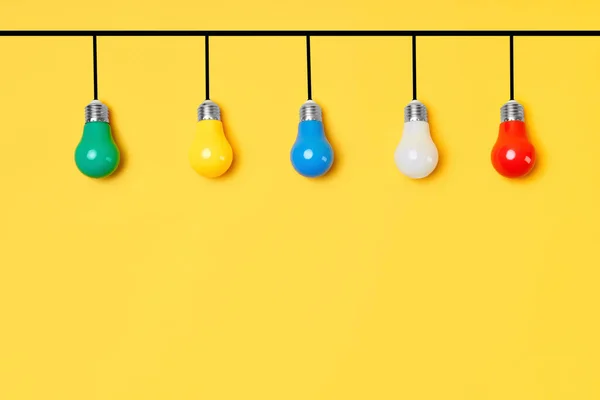 Creative layout with multicolored lightbulbs on yellow background — Stock Photo, Image