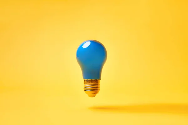 Blue lightbulb levitate on yellow background. Idea and inspiration concept — Stock Photo, Image