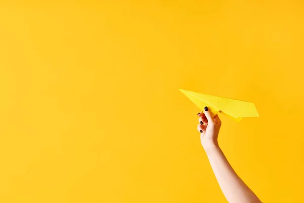 A womans hand holds paper airplane on yellow background