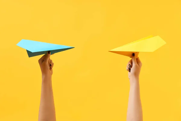 Женские руки держат разноцветные бумажные самолеты на желтом фоне — стоковое фото