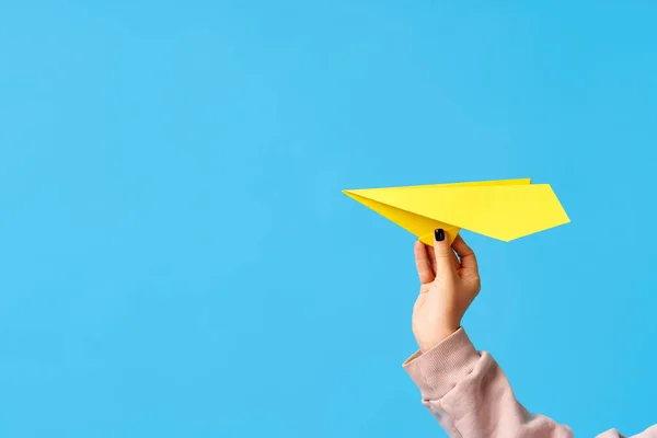 Bir kadının eli mavi arka planda sarı kağıt uçak tutuyor. — Stok fotoğraf