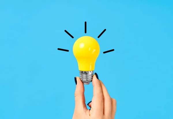 Female hand hold yellow light bulb on blue background — Stock Photo, Image