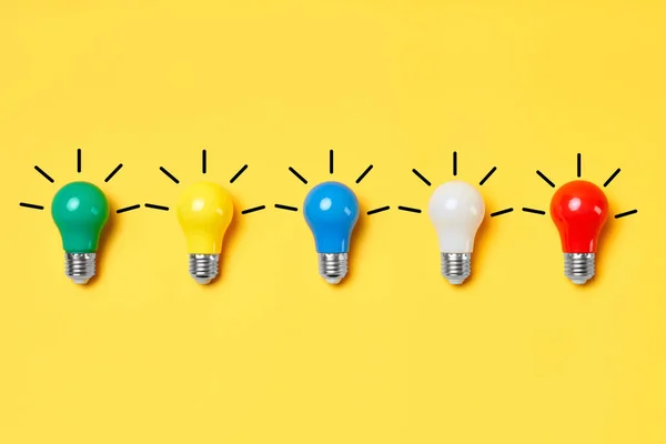 Creative layout with multicolored lightbulbs on yellow background. — Stock Photo, Image