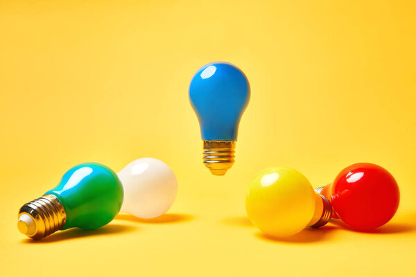 Creative layout with multicolored lightbulbs on yellow background. Blue light bulb levitate in air.