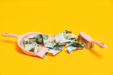 Faraş, el süpürgesi ve buruşuk para dolu sarı arka planlı yaratıcı bir düzen.