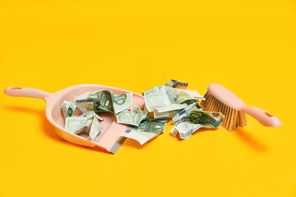 Creative layout with dustpan, hand brooms and crumpled money dollar bills on yellow background — Stock Photo, Image