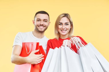 Young happy couple holding shopping bags in hands over yellow background