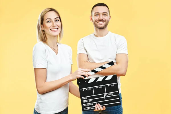 Young happy couple with cinema clapper board over yellow background — ストック写真