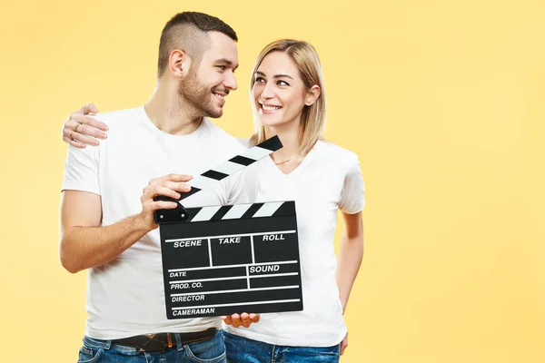 Young happy couple with cinema clapper board over yellow background — ストック写真