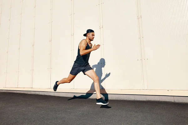 Young man runner running along wall with copy space — стоковое фото