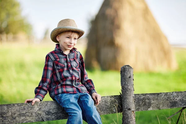 Retrato de cerca del niño con sombrero sentado en una valla de madera —  Fotos de Stock