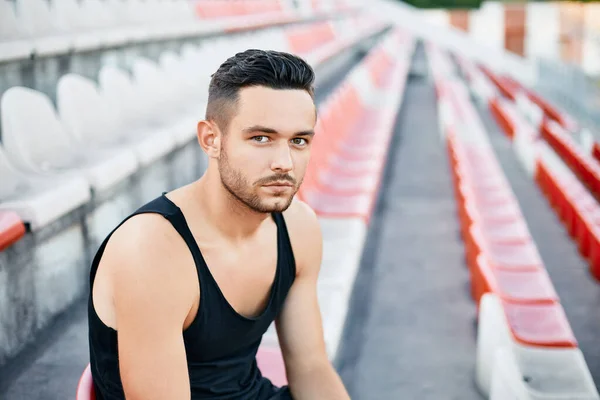 Handsome tired athlete relaxing on stadium stairs after workout — Stock Photo, Image