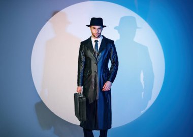 Siyah ceketli yakışıklı bir adam ve elinde çanta stüdyonun arka planında poz veriyor.