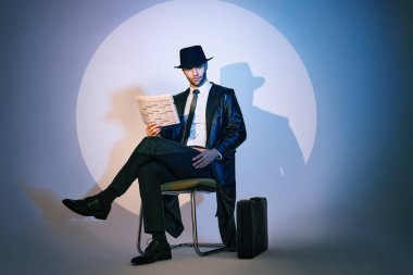 Sandalyede oturan yakışıklı özel dedektif stüdyonun arka planında gazete okuyor.