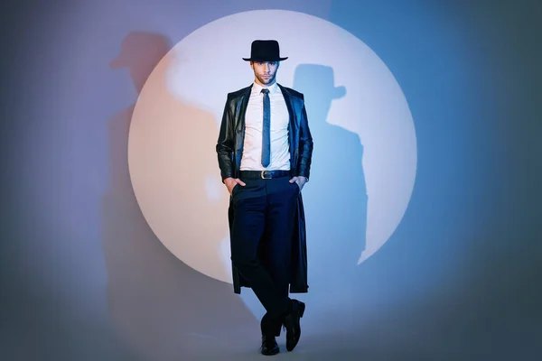 Full length portrait of handsome man in black coat and hat posing on studio in the spotlight — Stockfoto