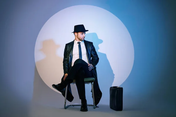 Handsome private detective sitting on chair in the spotlight on studio background — Fotografia de Stock