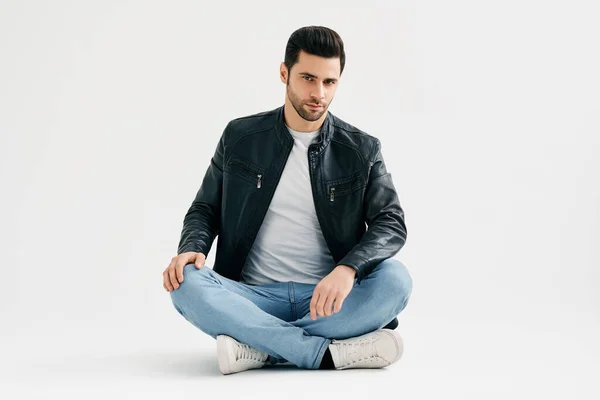 Przystojny modny człowiek siedzi na podłodze odizolowany na białym tle studio — Zdjęcie stockowe