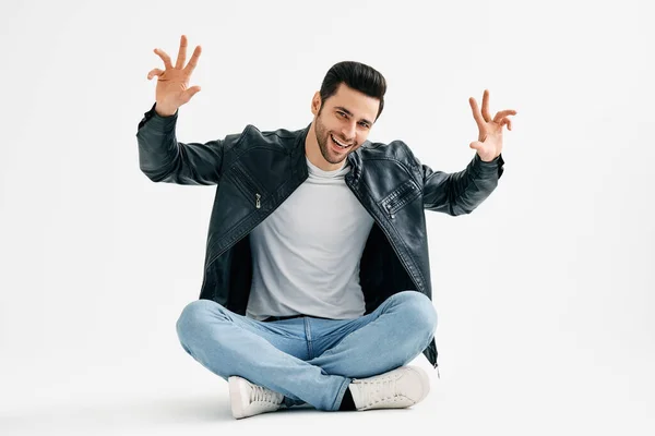 Positive smiling young man wave hands sitting with legs crossed on floor isolated over white background — Stok fotoğraf