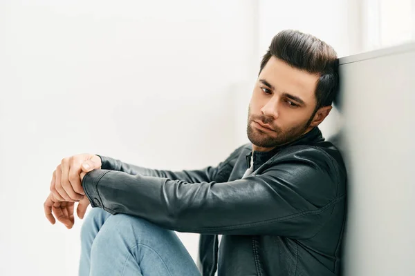 Portrait of handsome thoughtful man sitting on floor leaning to the wall — Stockfoto