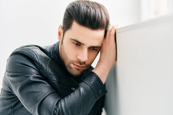 Portrait of handsome thoughtful man sitting on floor leaning to the wall — Stockfoto