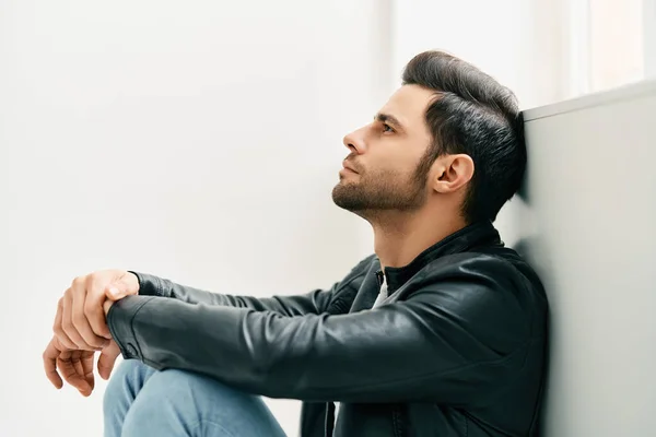 Portrait of handsome thoughtful man sitting on floor leaning to the wall — стоковое фото