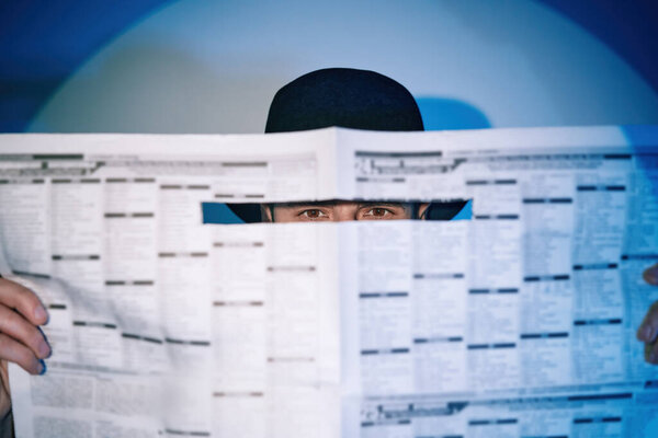 Man hiding watches through the newspaper in the spotlight on studio background Stock Picture