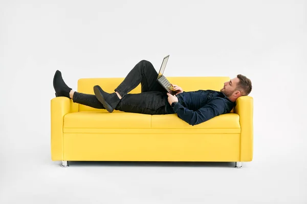 Relaks Człowieka Leżącego Żółtej Kanapie Przy Użyciu Laptopa Białym Tle — Zdjęcie stockowe