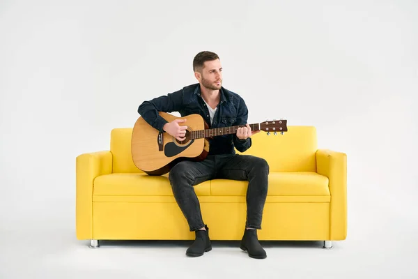 Handsome Young Man Playing Acoustic Guitar Whlile Sitting Yellow Sofa — Stock Photo, Image