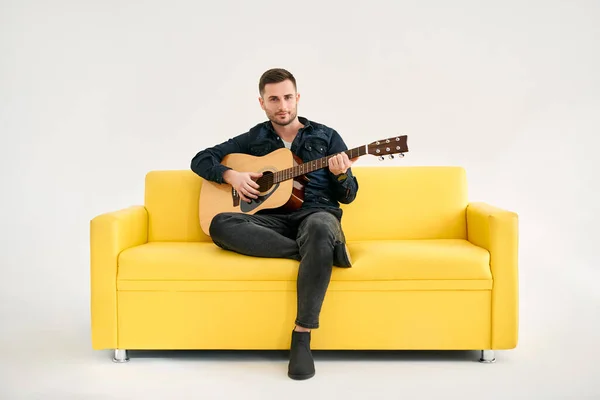 Joven Guapo Tocando Guitarra Acústica Mientras Está Sentado Sofá Amarillo —  Fotos de Stock