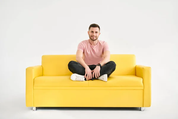 若い流行の男がカメラを探して黄色のソファに座ってポーズ リラックスしたコンセプト — ストック写真