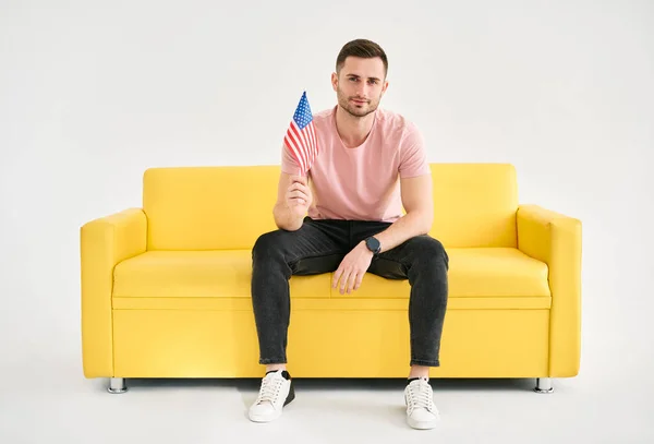 Joven Hombre Alegre Con Bandera Americana Mano Sentado Brillante Sofá —  Fotos de Stock