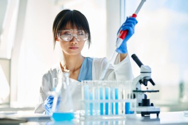 Modern kimya laboratuvarında çalışan pipet, matara ve test tüplerini kullanarak mikrobiyoloji araştırması yapan kadın bilim adamı. Tıp, biyoteknoloji konsepti