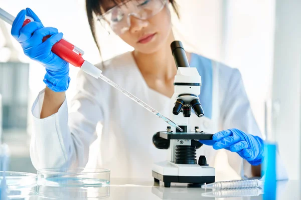 Modern bilim laboratuarında çalışan güzel kadın bilim adamı mikroskop slaytlarını hazırlıyor ve analiz ediyor. Kimya, Tıp, Biyoteknoloji konsepti