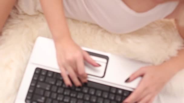 Девушка печатает на ноутбуке в белой кровати, видно сверху — стоковое видео