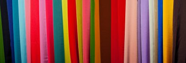 Renkli kumaşların dokusu yakınlaşıyor. Elbise dikmek için kumaşlar mağazada asılı. Farklı malzeme, renk ve dokulardan oluşan birçok kumaş.