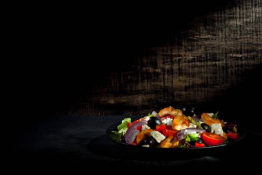 Domatesli salata, biber, zeytin ve tavuk filetosu. Siyah tabakta, siyah arka planda taze salata. Yemek yakınındaki metin için boşluk ve boş alanı kopyala.